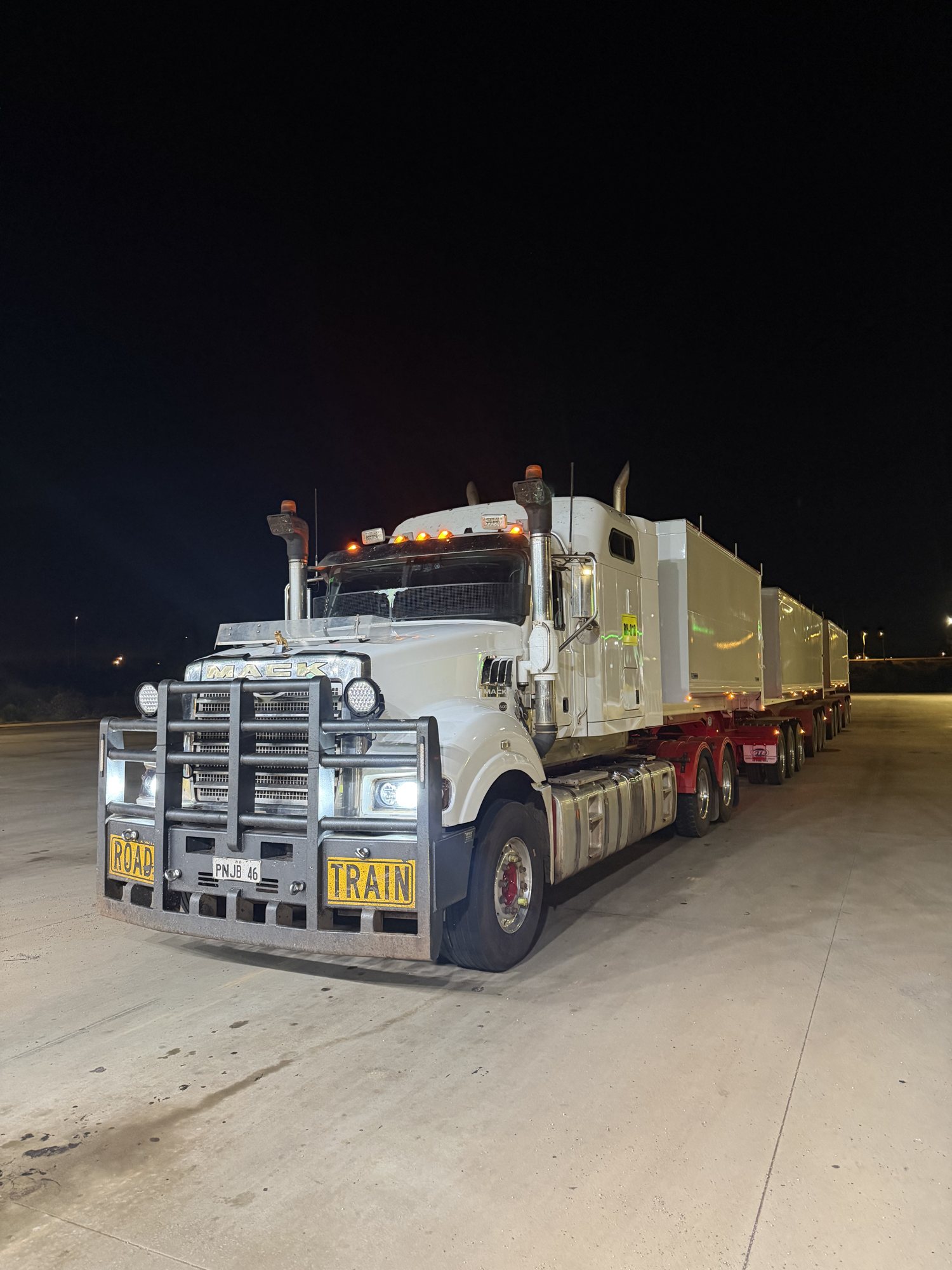 White Mack road train with three tipper trailers parked on a concrete pad at night