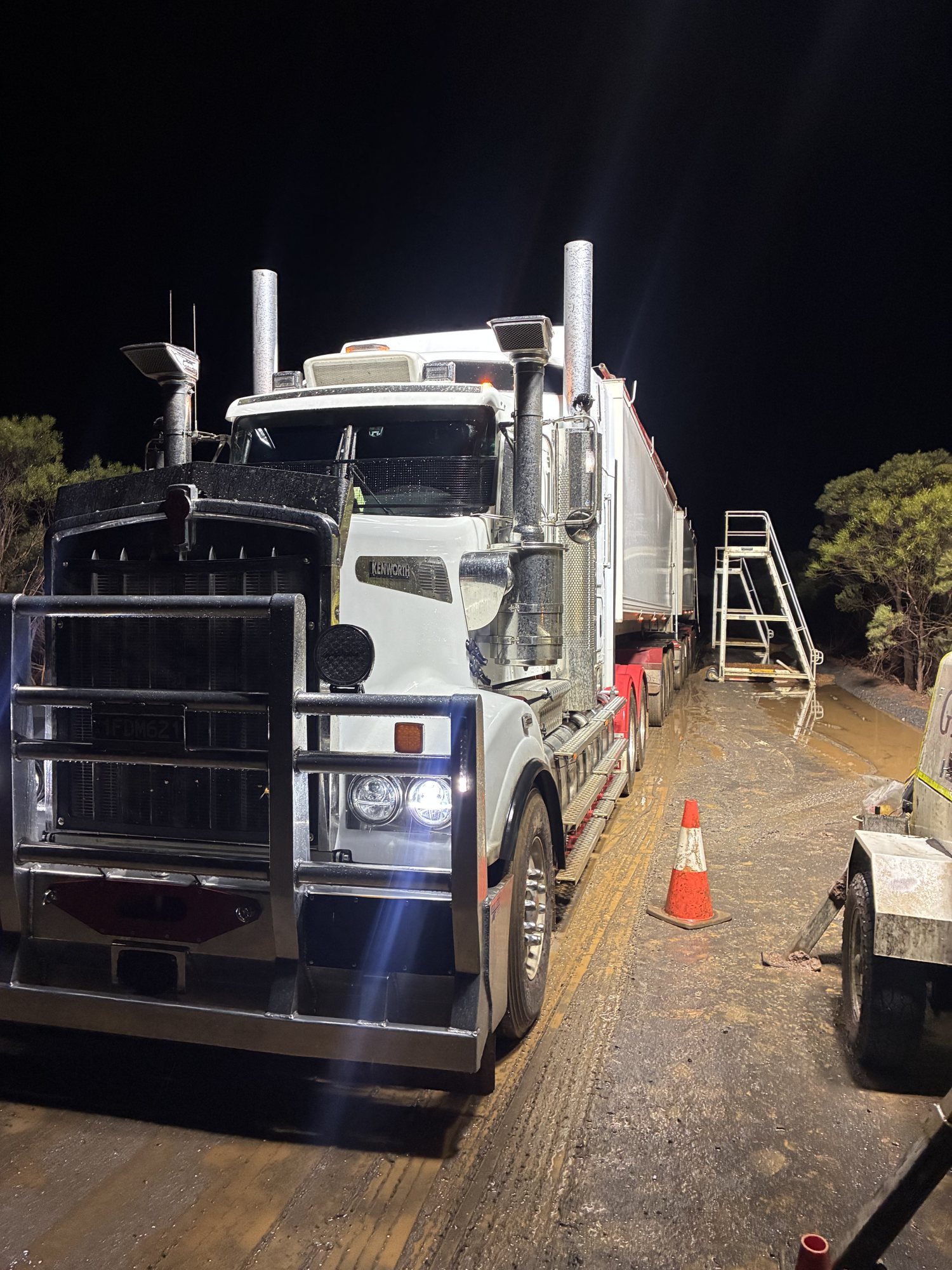 White Kenworth prime mover with bull bar and tipper trailer lit up at night